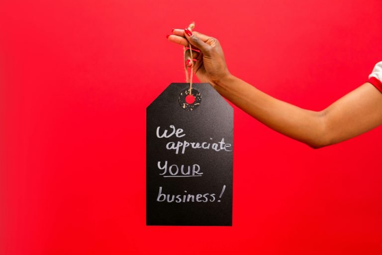a hand holding a large, black product tag saying 'We appreciate your business', against a red background