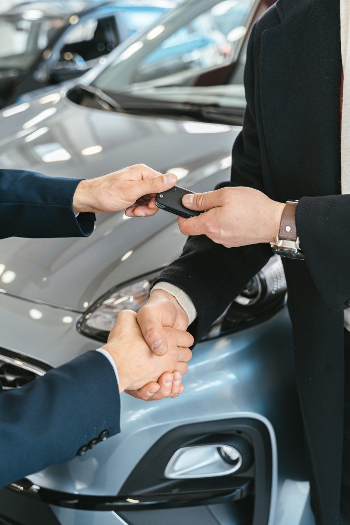 Two people handing car keys over to the other whilst shaking hands