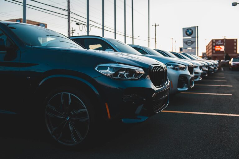 A row of new BMW SUVs parked on a dealership lot at sunset, with a prominent BMW logo sign in the back.