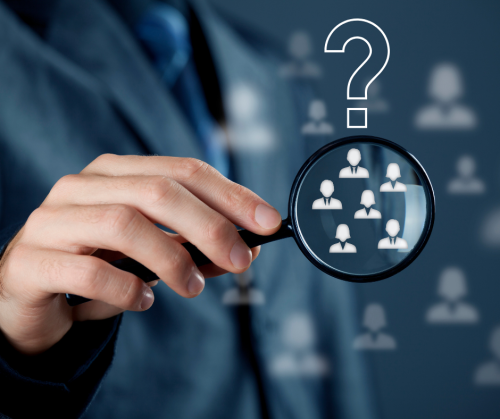 A person holding a magnifying glass, showing head shot images, which are blurred, outside the magnifying glass. There is a question mark above the magnifying glass.